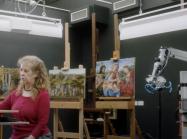 conservator looks at computer in front of several paintings
