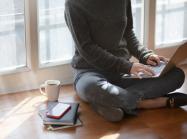 woman works on computer on the floor next to mug