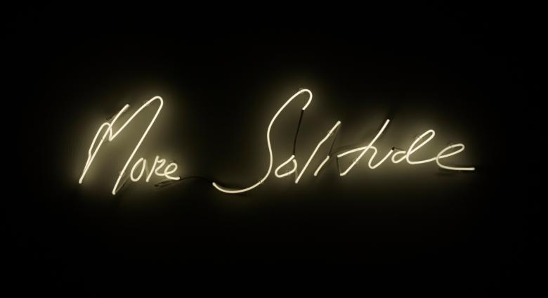 white Neon sign on a black background reading "more solitude"