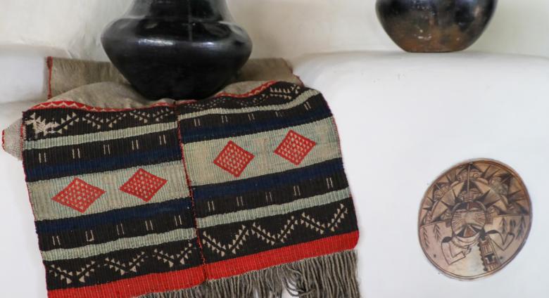 Hopi sash, ca. 1880–1890, 18.5 x 47 in. Two-piece handwoven embroidered sash sewn together with red yarn. White woven cotton fabric with weave of red, green, black, and white yarn wefts on white cotton warp. One panel longer, fringe. On a fireplace mantel in the Couse Home with northern New Mexico Pueblo pottery and a ceramic insert attributed to Nampeyo (Hopi). E. I. Couse Collection.