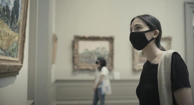 woman in mask looks at painting in the met