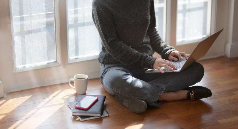 woman works on computer on the floor next to mug