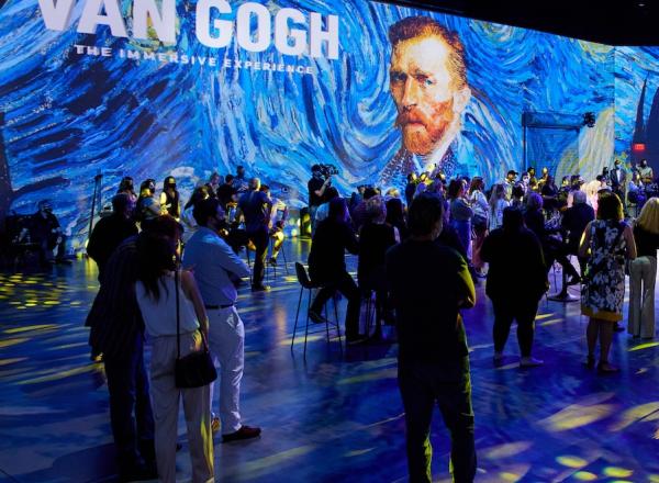View of Exhibition Van Gogh: The Immersive Experience at AREA15. The room is filled with people in VR goggles, the lighting on the crowd has brought starry night into the room, details of stary night are projected on the walls. 