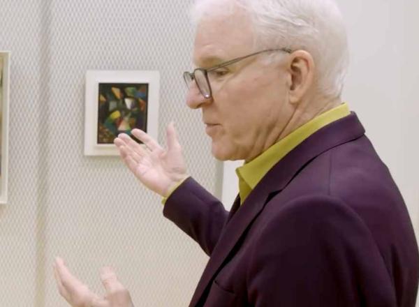 Steve Martin looks closely at work of art on wall